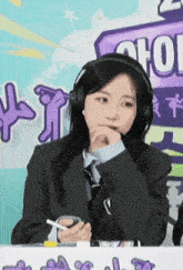 a woman wearing headphones and a suit is sitting at a table with a sign that says chool on it