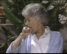 a woman with gray hair is sitting in front of a plant and holding her hand to her mouth .