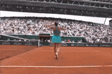 a woman in a blue dress is playing tennis on a court