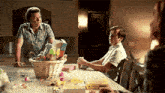 a man is standing next to a basket of easter eggs at a table .