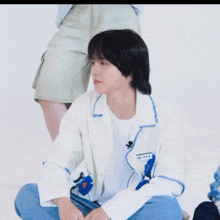 a young man wearing a white jacket with blue flowers on it is sitting on the floor with his arms outstretched