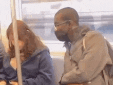 a man wearing a mask and glasses is sitting next to a woman on a train .