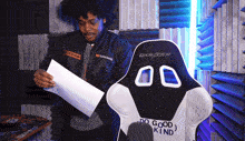 a man holding a piece of paper next to a chair that says dxracer