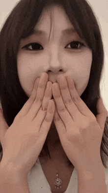 a woman covering her mouth with her hands while wearing a necklace with an e on it