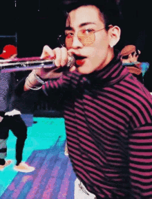 a young man wearing a striped shirt and sunglasses is holding a microphone in his mouth .