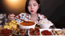 a woman is sitting at a table with bowls of food and a bowl of soup