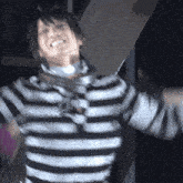 a man in a black and white striped shirt is smiling with his arms outstretched