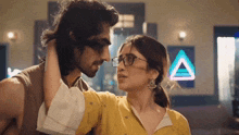 a man and a woman are looking into each other 's eyes with a neon triangle in the background