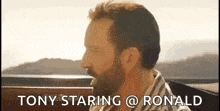 a man with a beard is sitting in a car with the words `` tony staring @ ronald '' written on the screen .
