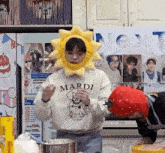 a person wearing a sun hat and a mardi sweatshirt is holding a stuffed strawberry .