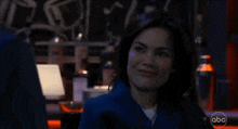 a woman is smiling in a dark room with a abc logo in the corner