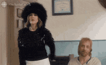 a man and a woman are standing next to each other in a room . the woman is wearing a fur hat .