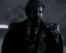 a man with a beard wearing a suit and tie is standing in the dark