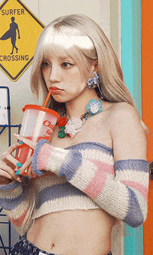 a woman drinking from a cup with a straw in front of a sign that says " surfer crossing "
