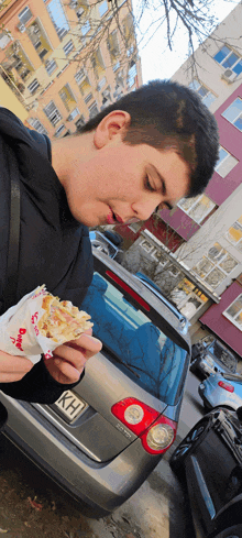 a young man eating a sandwich in front of a car with kh on the license plate