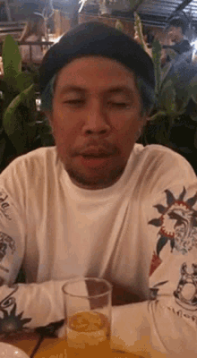 a man with blue hair is sitting at a table with a glass of beer and making a funny face .