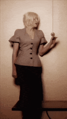 a woman in a grey jacket and black skirt is holding a pendulum in her hand