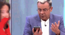 a man in a blue suit and glasses is looking at his phone