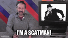 a man with a mustache is sitting in front of a television and says i 'm a scatman