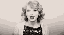 taylor swift is wearing a black dress and a white cardigan and waving at the camera in a black and white photo .