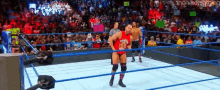 a wrestler in a red shirt stands in the middle of a wrestling ring in front of a crowd