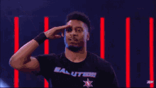a wrestler wearing a salute t-shirt is saluting in front of a crowd .