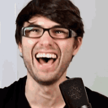 a man wearing glasses and a black shirt is holding a microphone and smiling