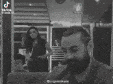 a man with a beard is sitting in front of a woman who is standing behind him