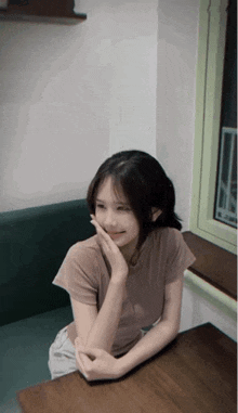 a young woman sits at a table with her hand on her face