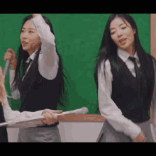 two girls standing in front of a green board