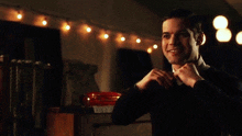 a man in a tuxedo and bow tie is standing in front of a string of lights ..