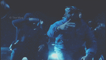 a man in a blue jacket is standing next to another man in a black hoodie with the name the maw on the bottom