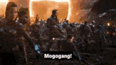a group of people are standing in front of a fire and a sign that says `` mogogang '' .