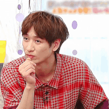 a man wearing a red plaid shirt is holding his hand to his chin