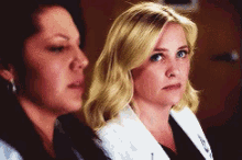 two women sitting next to each other with one wearing a white coat with the letter a on it