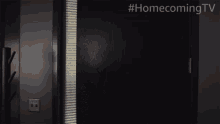 a woman is standing in a dark room with #homecomingtv written on the bottom