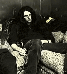 a man with long hair is sitting on a couch holding a microphone