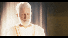 a man with a white beard and a white robe is standing with his eyes closed