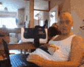 a man in a white tank top sits in front of a laptop computer