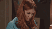 a woman with red hair and a blue shirt is looking at the camera