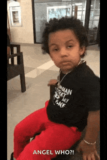 a little boy wearing a black shirt and red pants is sitting on a bench .