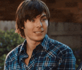 a young man wearing a blue plaid shirt is smiling