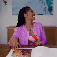 a woman in a purple cardigan is sitting at a table looking at a book .