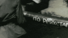 a black and white photo of a person laying on the ground with russian writing on a piece of paper