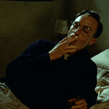 a man wearing glasses is laying on a bed holding a glass