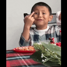 a young boy is giving the middle finger while sitting at a table .