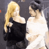two women are standing next to each other and one of them is holding a microphone