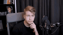 a young man sits in front of a microphone with the word me behind him