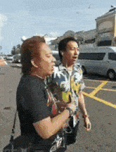 two men are walking down a street and one of them is wearing a hawaiian shirt .