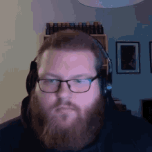 a man with a beard and glasses is wearing headphones and looking at the camera .